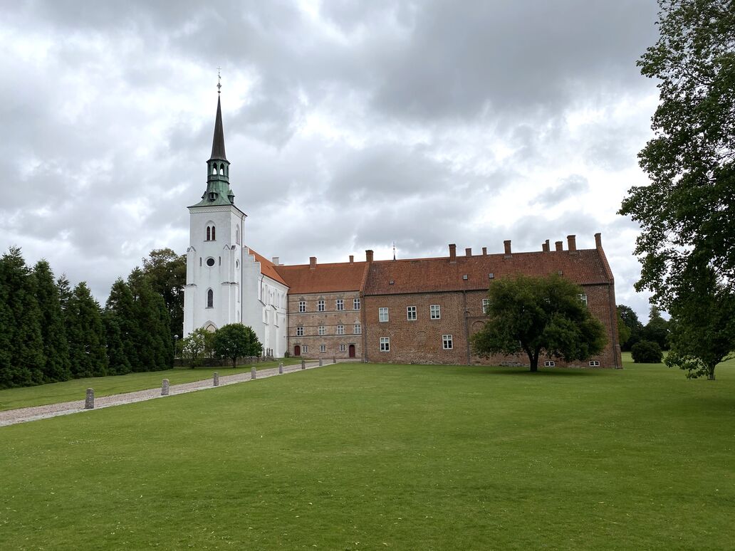 Brahetrolleborg set fra græsplæne i let frøperspektiv. Kirke til venstre i billedet bygget sammen med herregården til højre.